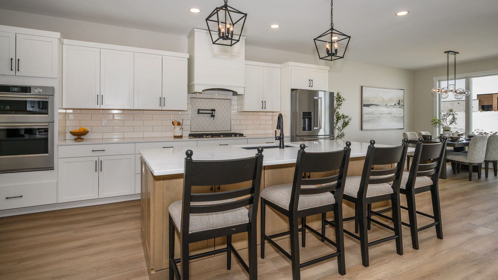 A Huntington Builders kitchen with white cabinets, a wood island, black fixtures and an adjoining dining area.